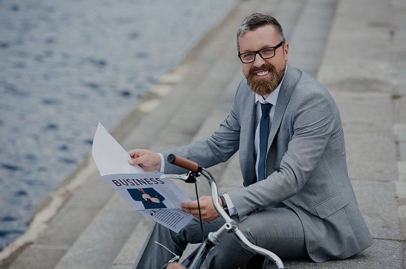 Businessman in gray suit reading business newspaper by the waterfront
